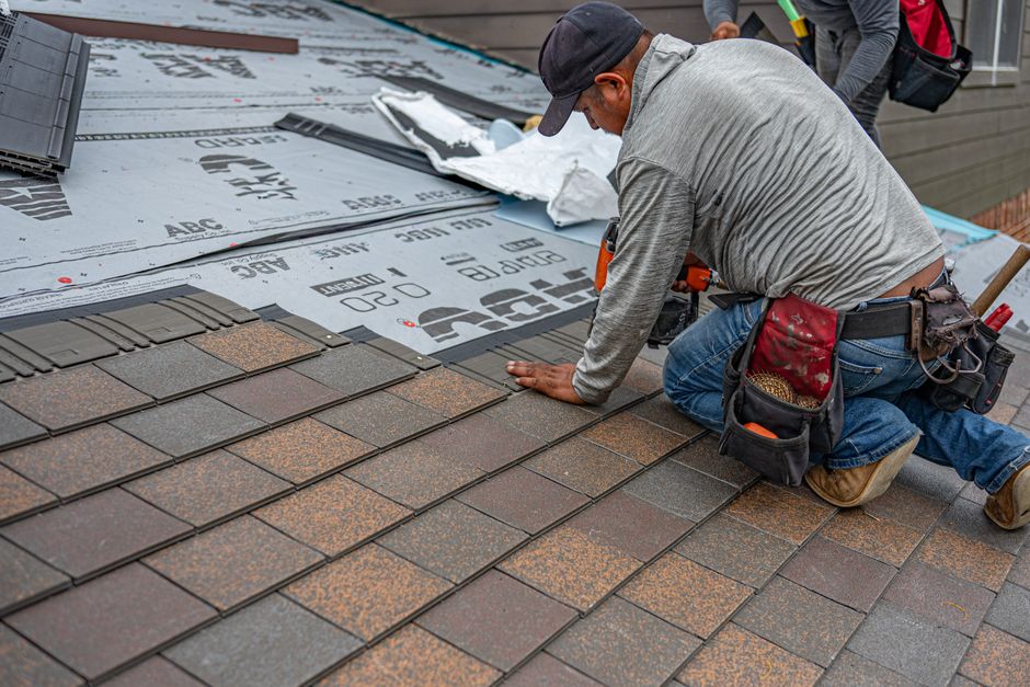 A roofer laying asphalt shingles on a residential roof.